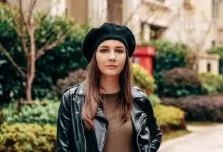 woman in black leather jacket and brown hat standing near green plants during daytime